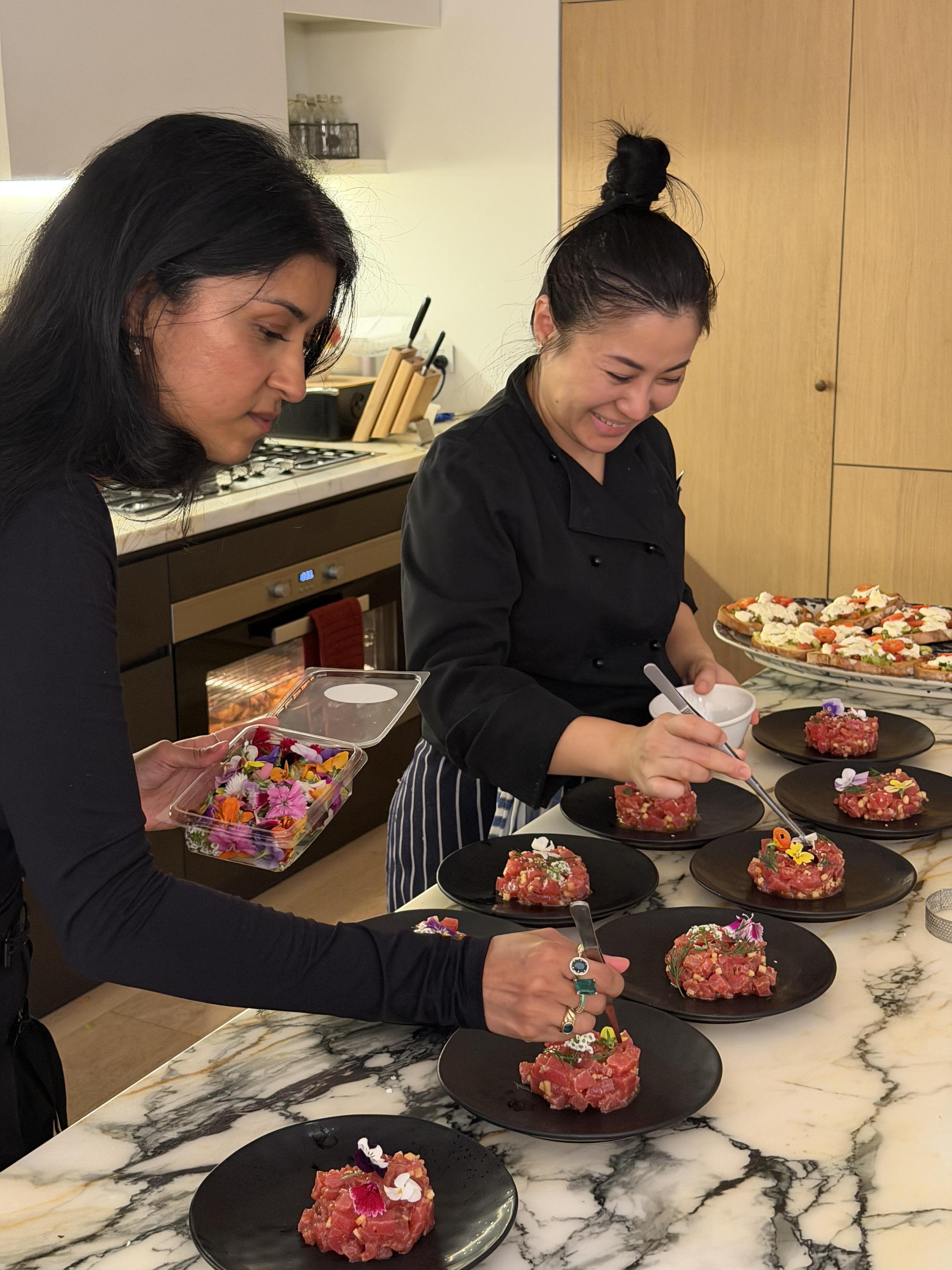 Two ladies garnishing raw tartare with edible flowers on black plates